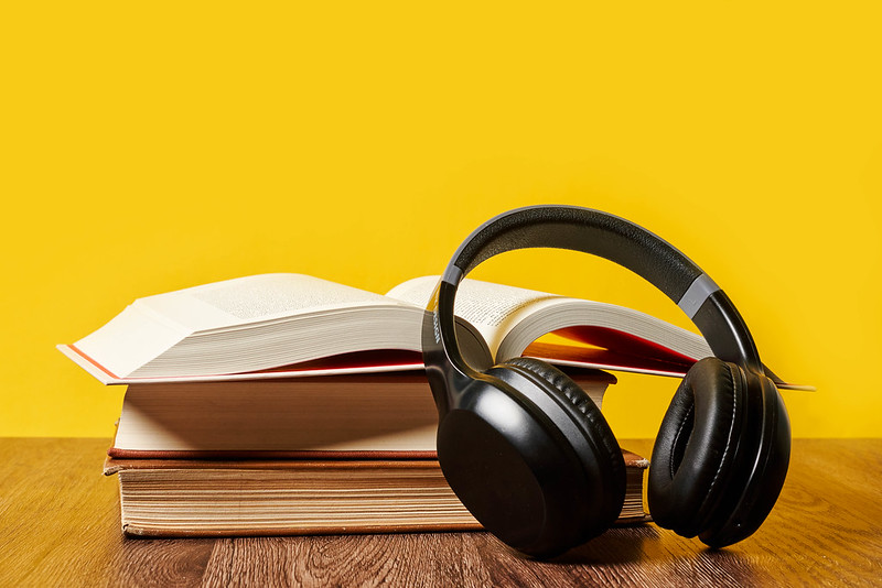 A stack of books, the top one open, with a pair of headphones resting against them.